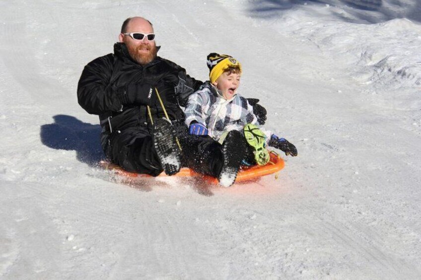A person and a child sledding down a snowy slope. 1