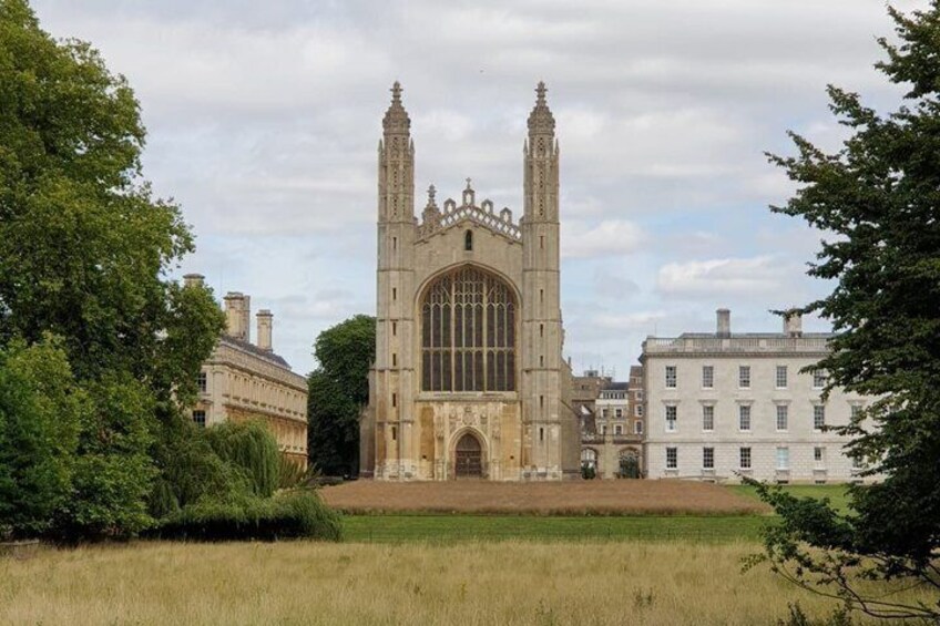 A historic building with twin towers and a large arched window, surrounded by trees and a grassy field. 1
