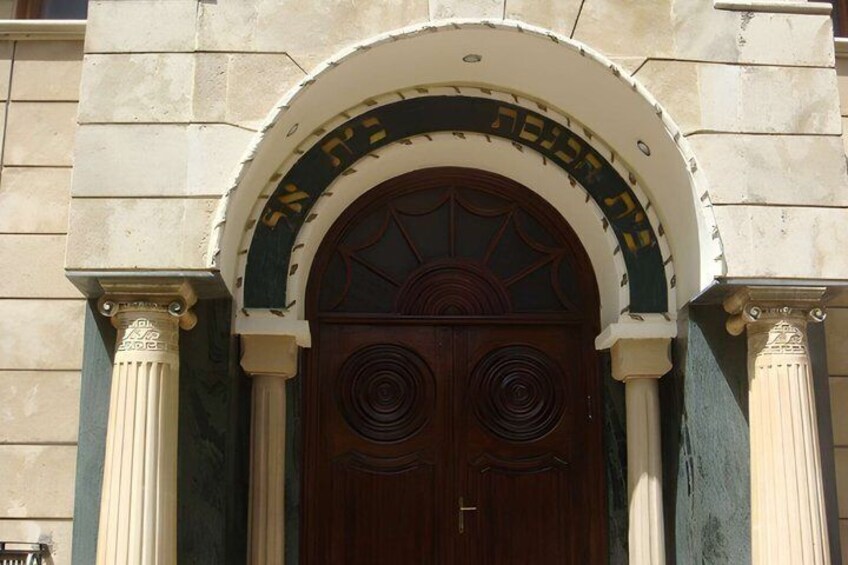 A building entrance with a large wooden door, an arched overhang, and Hebrew inscriptions. 3