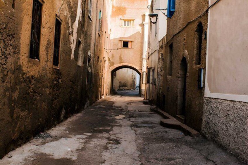 A narrow alleyway with old buildings, a visible archway, and a cobblestone path. 1