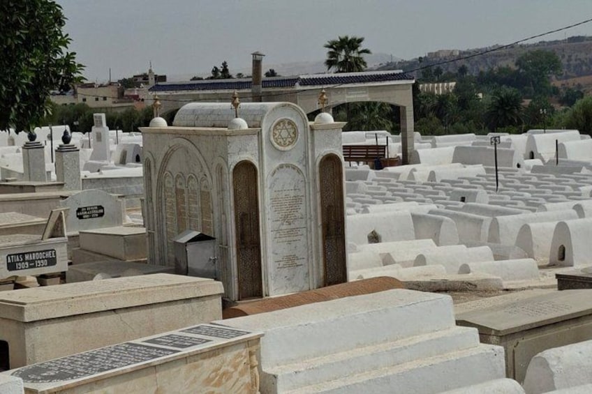 A cemetery with white tombstones and a central monument with inscriptions. 5