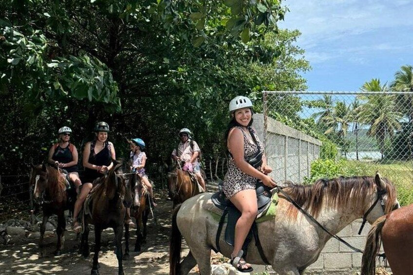 People riding horses along a path surrounded by trees and a fence. 4