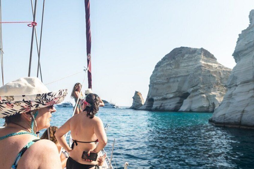 A sailboat with people on board, a rocky coastline, and clear blue water. 5