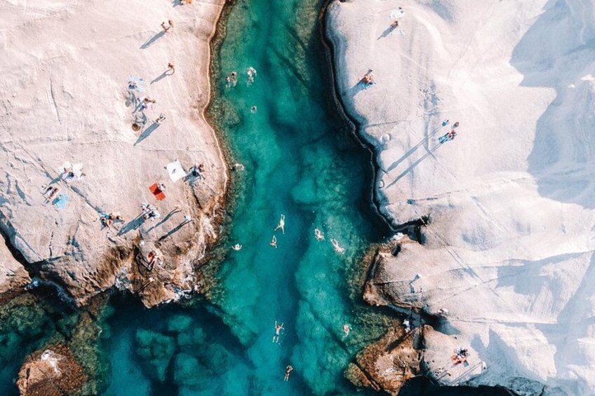 An aerial view of a beach with clear turquoise water, rocky terrain, and people sunbathing. 4