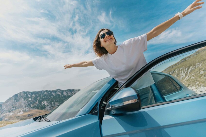 A person with arms outstretched, leaning out of a car window, with a mountainous landscape in the background. 5