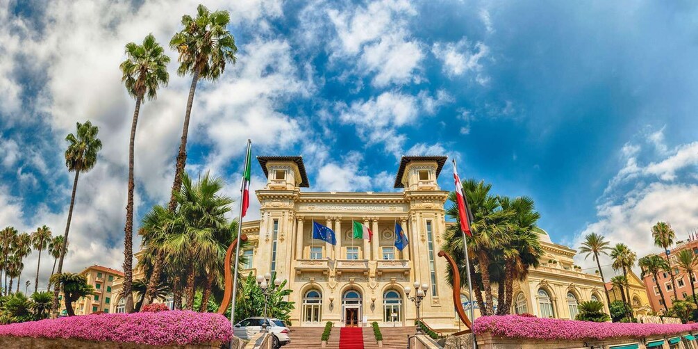 A grand building with columns and flags, surrounded by palm trees and pink flowers. 4