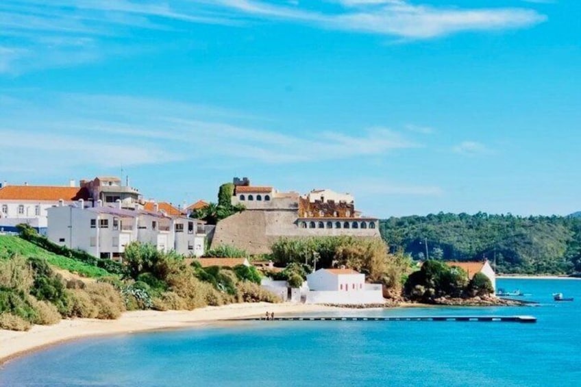 A coastal town with white buildings, a fort, and a clear blue sea. 4