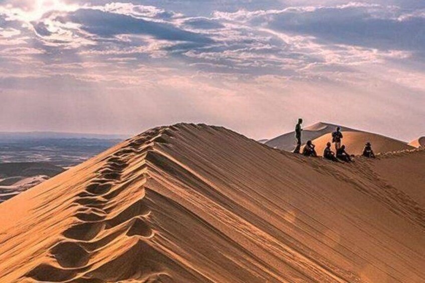 A desert landscape with sand dunes and people sitting on them. 5