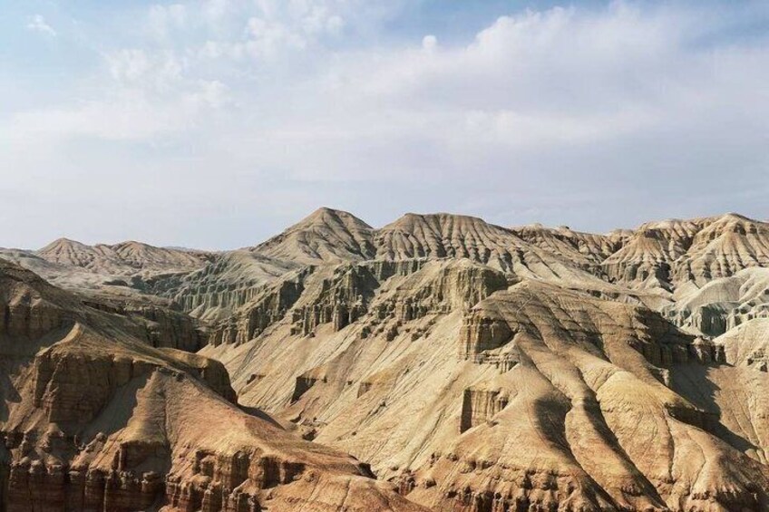 A rugged, eroded landscape with layered rock formations and a clear sky. 3