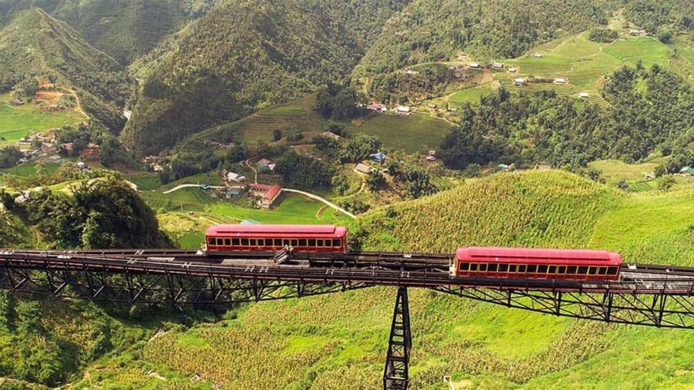 A red train on a bridge over a hilly landscape with fields and houses. 1