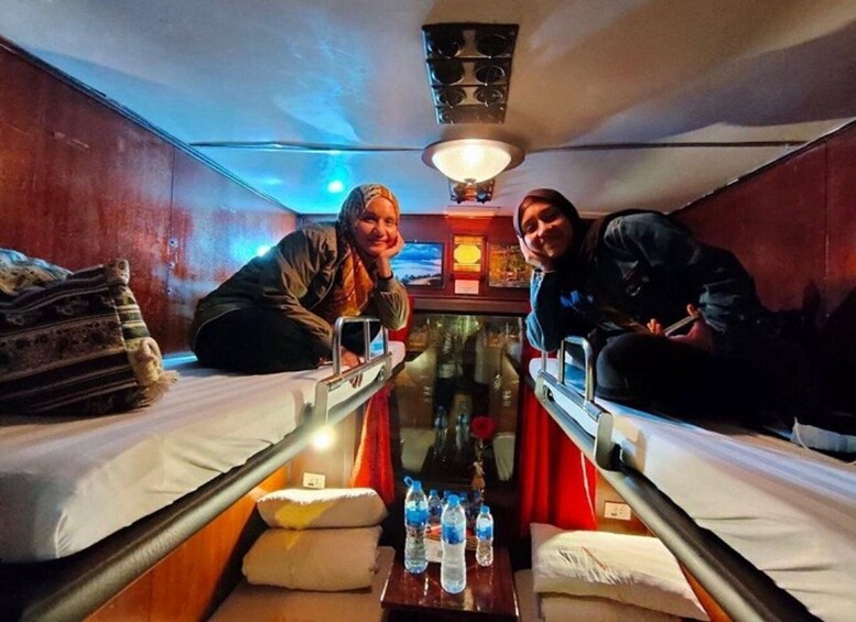 A narrow train compartment with two bunks, a table with bottles, and a ceiling light. 4