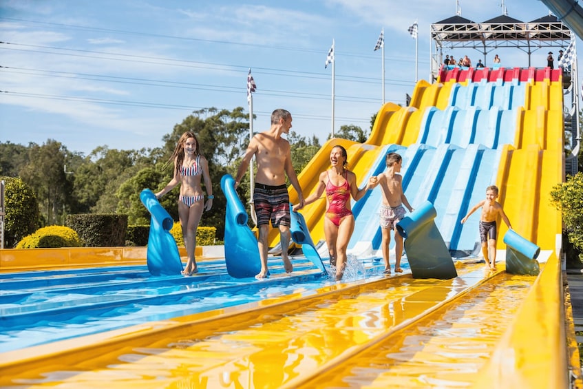 A water park with a large yellow and blue water slide and inflatable dolphins in the pool. 4