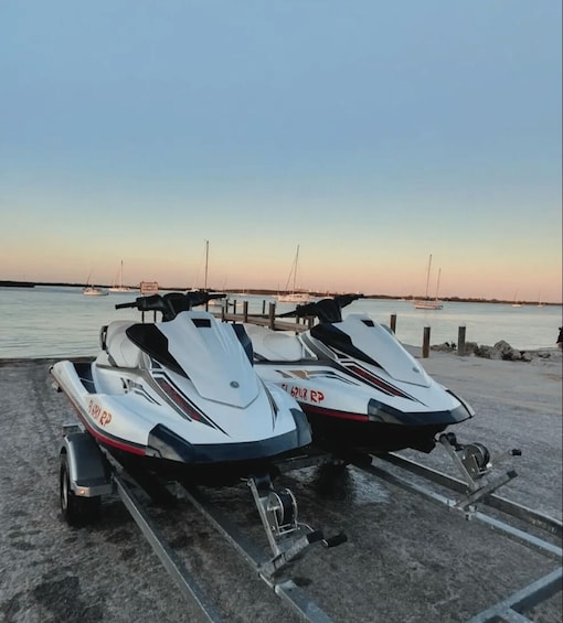 Two jet skis on trailers at a marina with boats in the background. 1