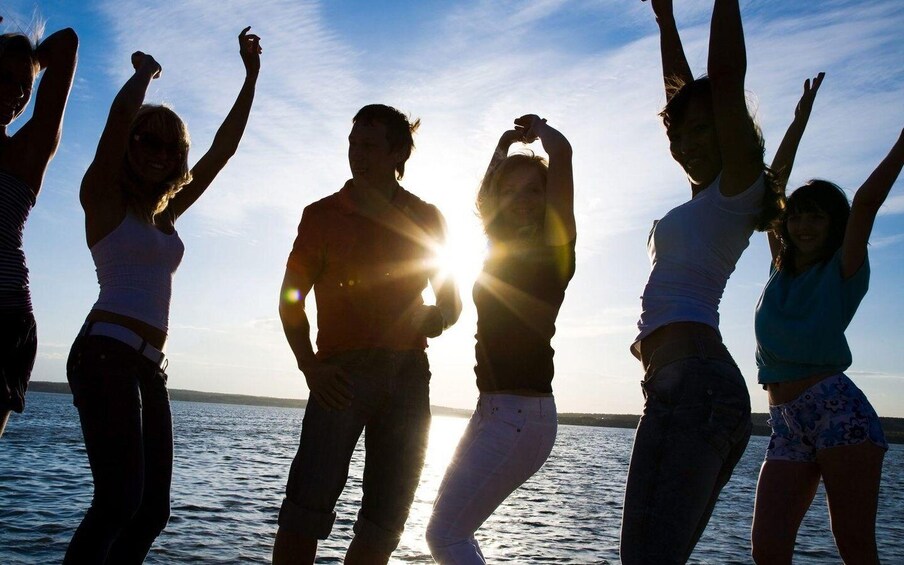 A group of people dancing by the water at sunset. 4