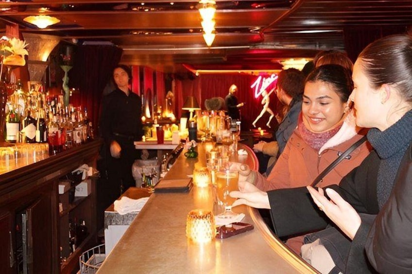 A bar with a long counter, bottles, and a neon sign in the background. 2