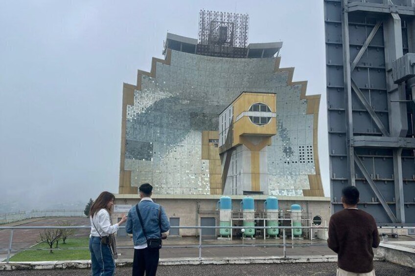 A large, reflective building with a unique geometric design, a staircase, and a fence in the foreground. 5