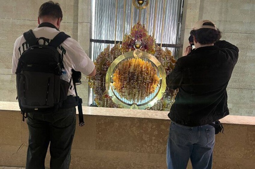 Two people taking photographs of a circular display with hanging items. 1