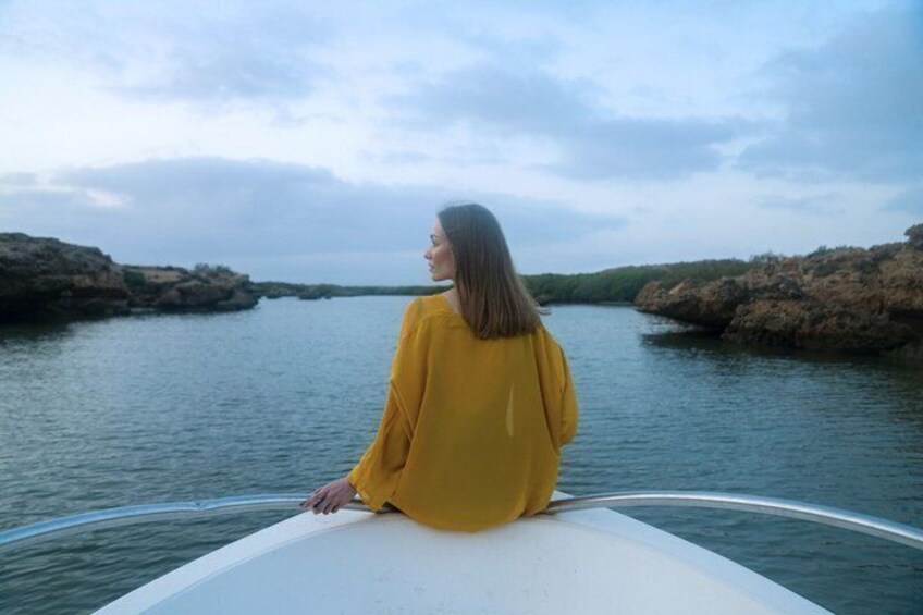 A person in a yellow top sitting on a boat's edge, overlooking calm water with rocky shores. 2