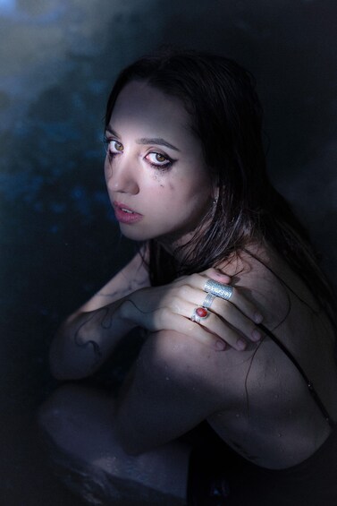 A person with tattoos and a ring, in a dimly lit environment. 2