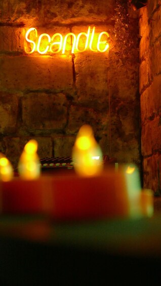 A neon sign reading 'scandle' against a brick wall with candles in the foreground. 1