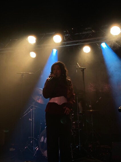 A person on stage with a microphone, stage lights, and musical instruments. 3
