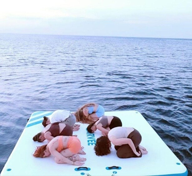 A group of people performing yoga on a floating platform in the ocean. 4