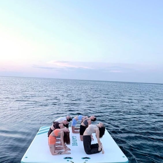 A group of people performing yoga on a floating platform in the ocean. 3