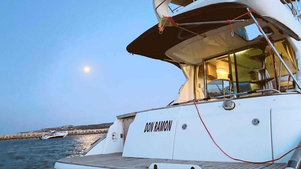 A boat named 'DON RAMON' docked at a harbor with calm waters and a clear sky. 5