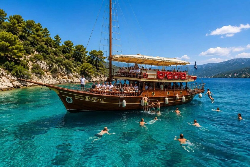 A boat named 'BENETIA' with people swimming in the water and a rocky coastline in the background. 3