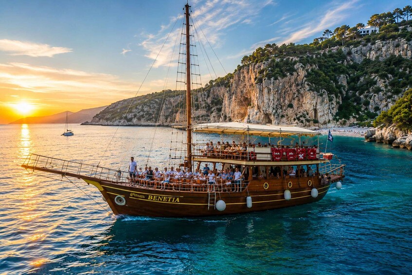 A wooden boat named 'BENETIA' with passengers, sailing near a rocky coastline at sunset. 1