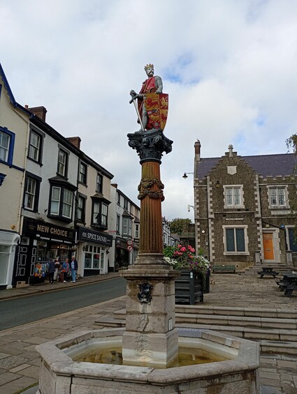 A statue of a king on a pedestal in a town square with shops and a police building in the background. 5