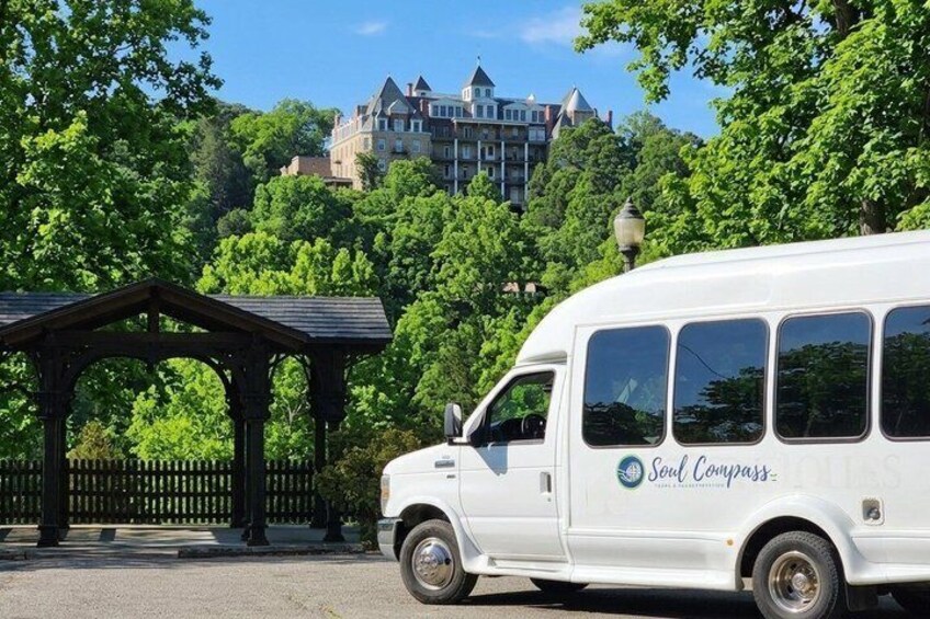 A white van with 'Soul Compass' written on it, parked in front of a gazebo with a large building in the background. 1