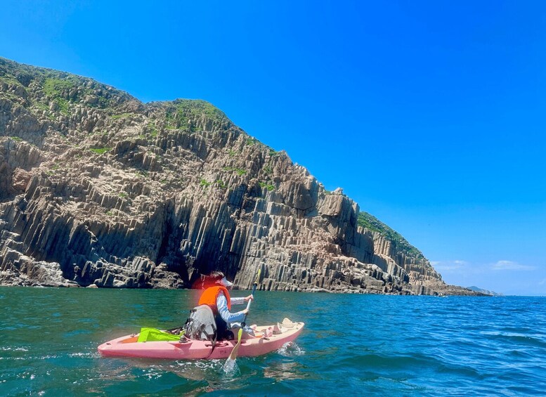 A person kayaking on clear blue water with a rocky cliff in the background. 2