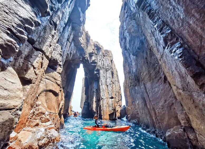 A kayaker navigating through a narrow canyon with towering rock formations. 1