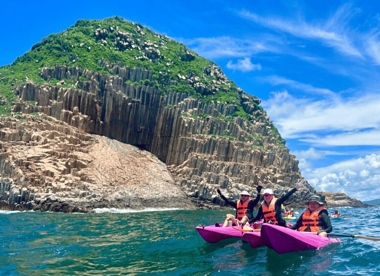 People kayaking on turquoise water with a rocky cliff and lush greenery in the background. 3