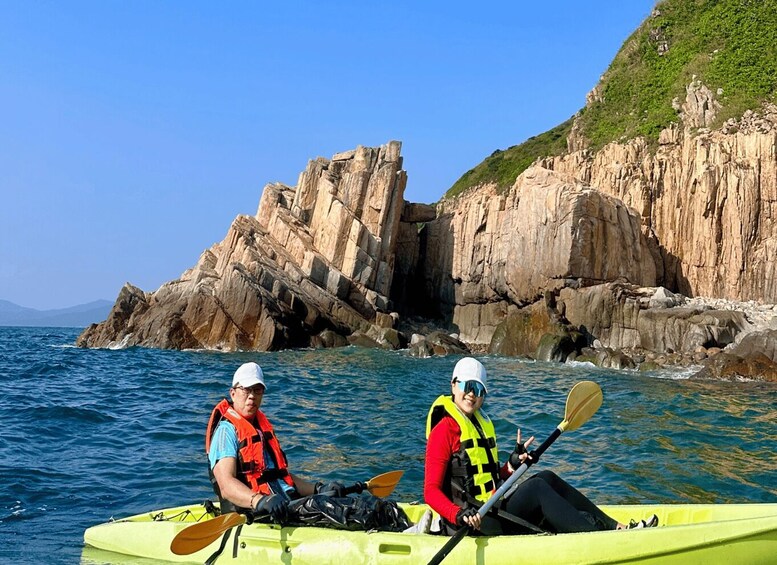 Two people kayaking on a calm sea with rocky cliffs in the background. 5