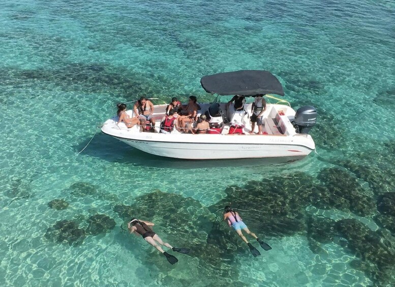 A boat with passengers and two snorkelers in clear turquoise water. 1