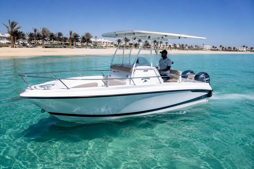 A white speedboat with a canopy, moving through clear turquoise water near a sandy beach with palm trees. 3