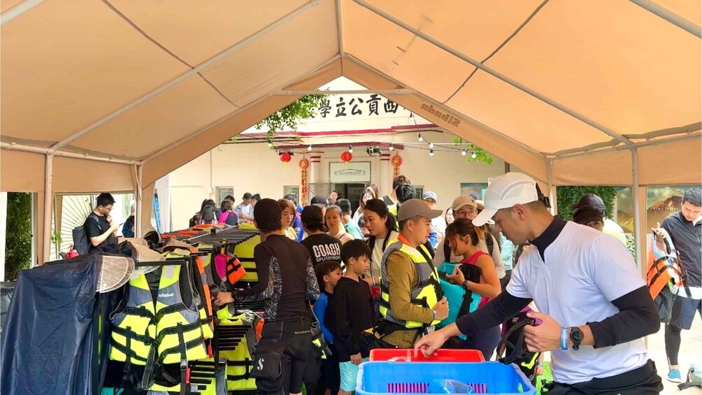 A group of people under a tent, some wearing life jackets, and a sign with Chinese characters. 4