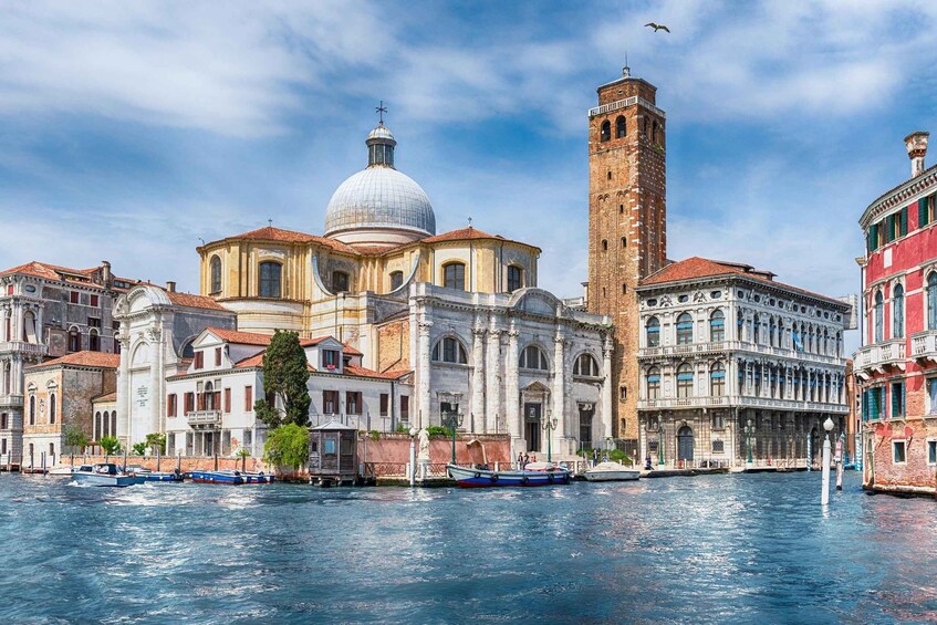 A historic Venetian building with a prominent dome and adjacent tower, surrounded by water and classic architecture. 1
