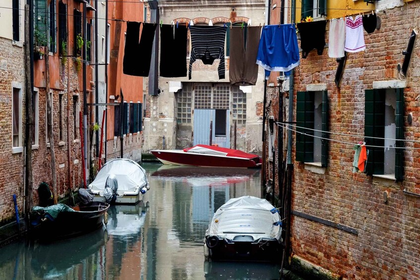 A narrow canal with boats, laundry hanging on a line, and brick buildings. 2