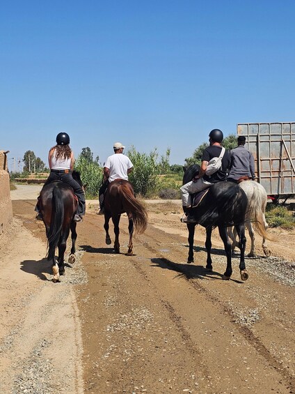 Four people riding horses on a dirt road with a trailer in the background. 5