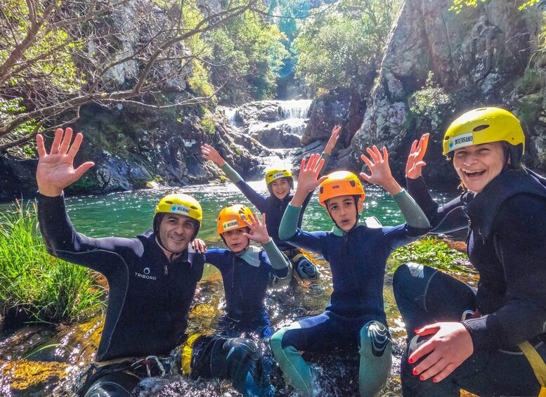 A group of people in wetsuits and helmets by a waterfall in a forested area. 1
