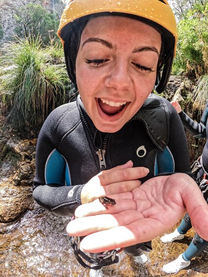 A person wearing a helmet and a wetsuit, holding a small frog in their hand. 3