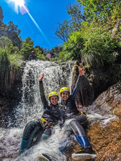 Two people in helmets and wetsuits sliding down a waterfall. 2