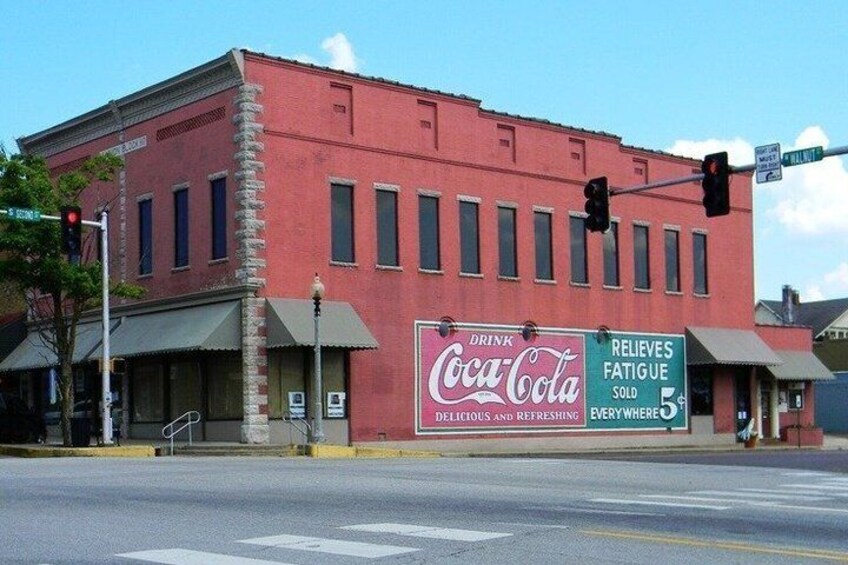 A red brick building with a Coca-Cola billboard and a sign stating 'Relieves Fatigue Sold Everywhere.' 2