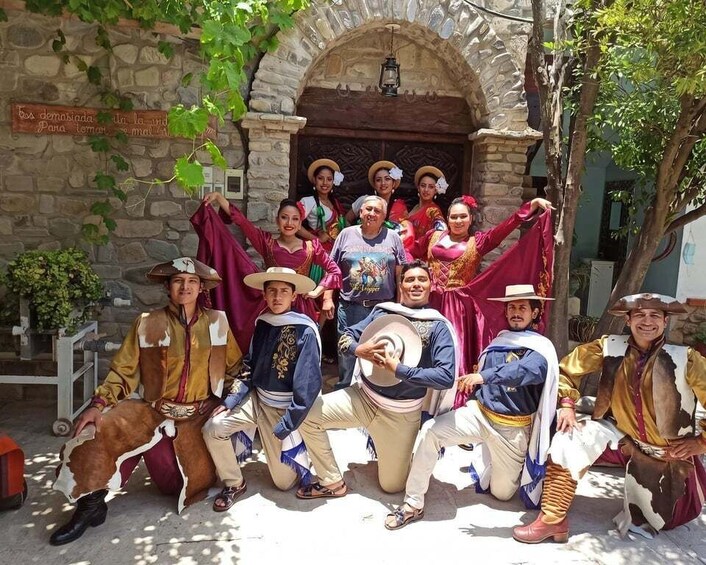 A group of people in traditional costumes posing in front of a stone building with a sign. 5