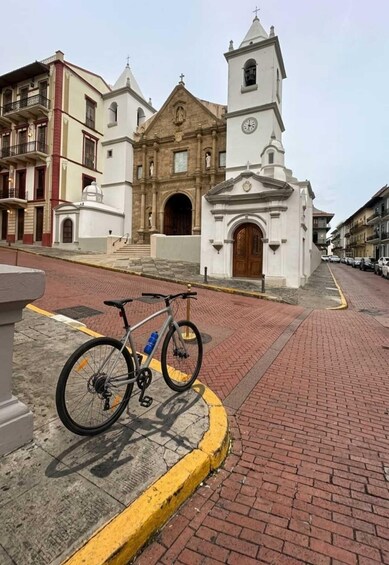 A historic church with a bell tower, a bicycle parked on the sidewalk, and a paved street. 5