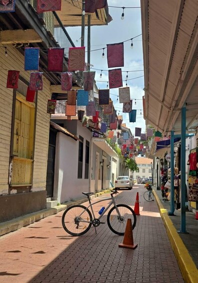 A street with colorful hanging textiles, a parked bicycle, and a white car in the distance. 4