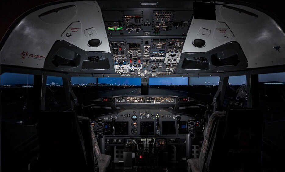 The interior of an aircraft cockpit with multiple control panels, emergency exits, and a view of the runway at night. 3